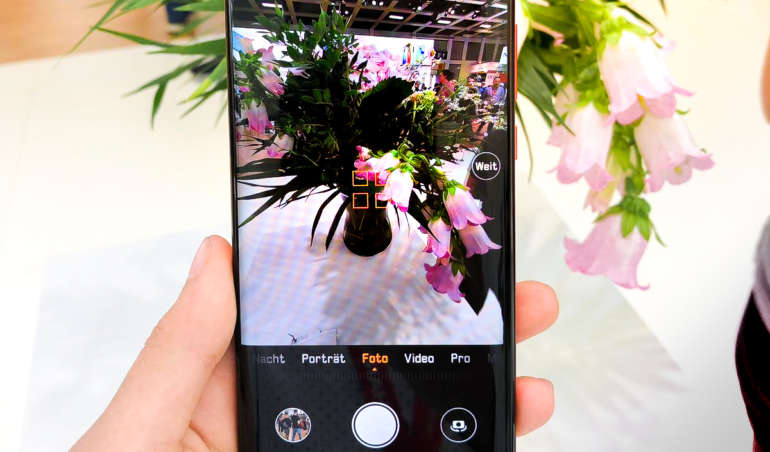 Das Huawei P30 mit geöffneter Kamera wird vor eine Blumenvase gehalten