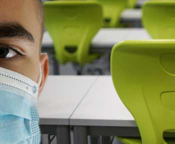 Schüler mit Maske steht in einem Klassenraum
