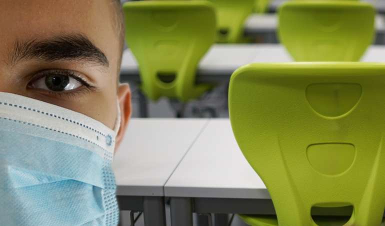 Schüler mit Maske steht in einem Klassenraum