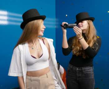 Lilly und Ronja stehen vor einer blauen Wand und filmen sich gegenseitig.